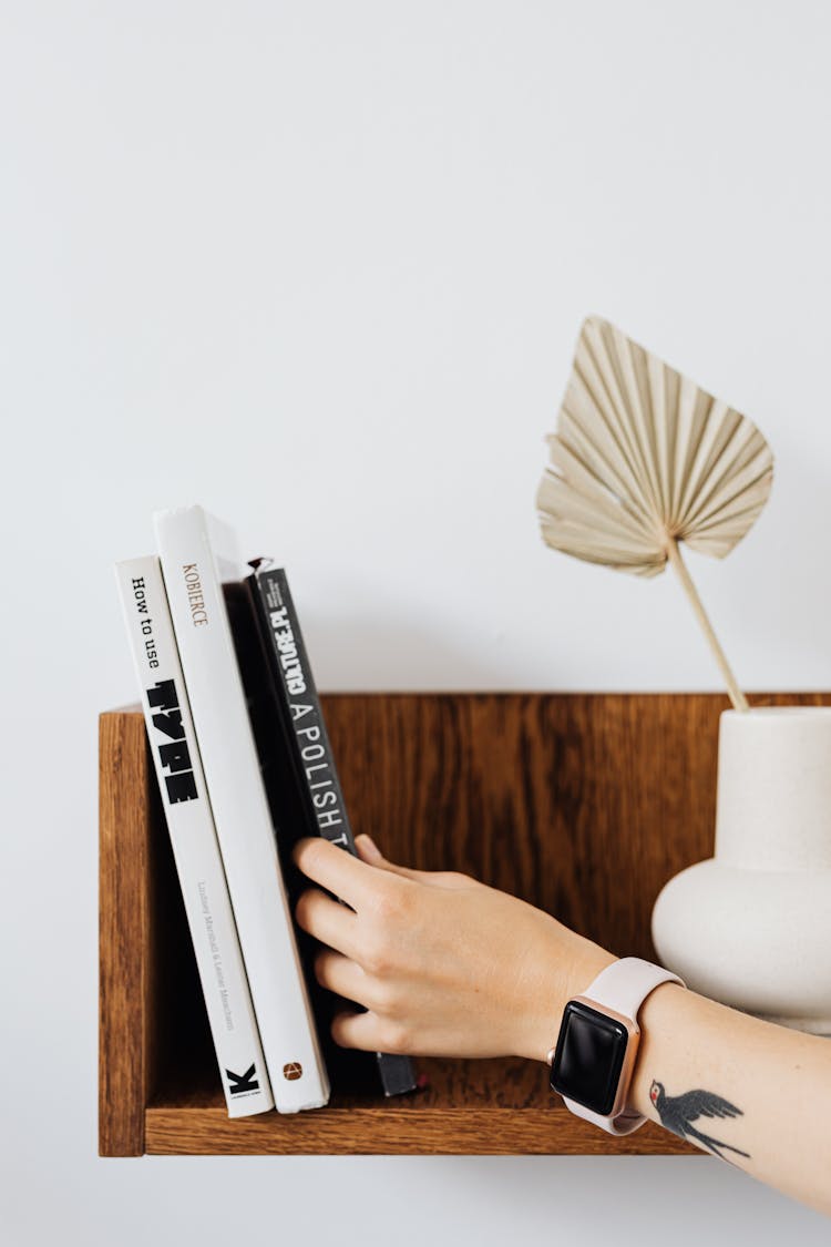 Close Up Of Hand Reaching For Book On Shelf