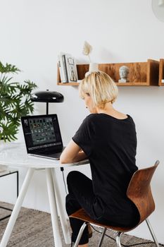 Blonde woman using laptop at home office desk, showcasing remote work lifestyle.