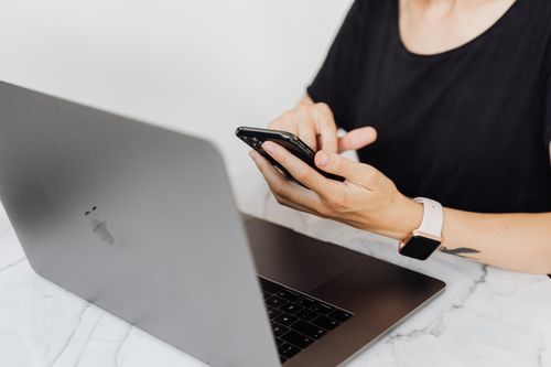 Free Close-up of woman using smartphone and laptop at desk, wearing a smartwatch. Stock Photo