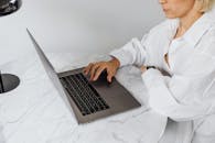 一位穿着白衬衫的白人妇女坐在室内的大理石桌子前用笔记本电脑工作