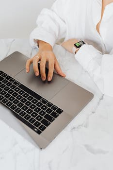 A person using a laptop with a smartwatch on a marble table, showcasing modern technology.
