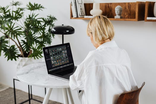 Blonde woman using laptop at white marble table with decor and plant.