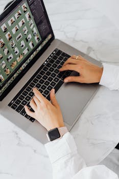 Hands typing on a laptop with smartwatch on marble desk, showcasing modern technology.