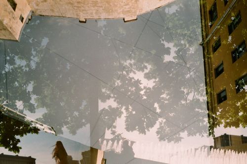 Free Surreal reflection of buildings, trees, and fountain in a glass surface. Stock Photo
