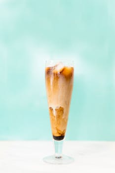A tall glass of iced coffee with cream swirls on a bright blue background, perfect for a summer refreshment.