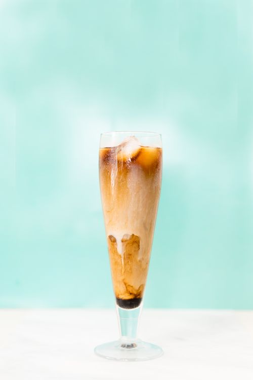 Free A tall glass of iced coffee with cream swirls on a bright blue background, perfect for a summer refreshment. Stock Photo