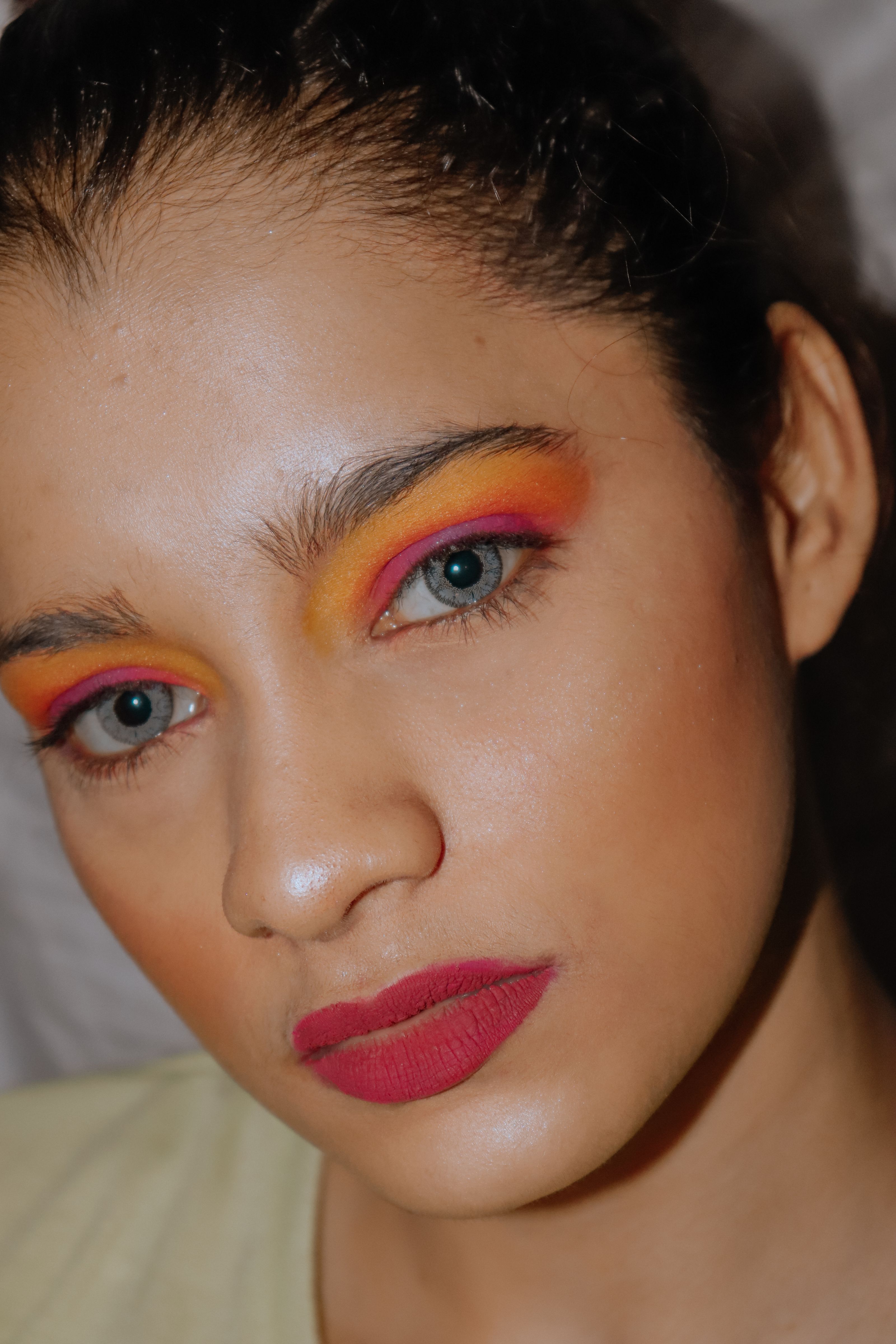 Retrato em close de uma mulher com maquiagem vibrante nos olhos e batom vermelho, destacando tendências de beleza ousadas.