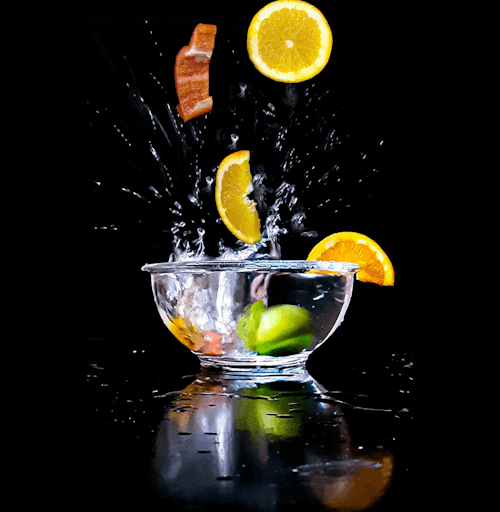 Dropping Slices Of Orange and Bell Peppers on a Glass Bowl