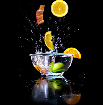 Dynamic citrus fruits splashing into a glass bowl with water against a black background.