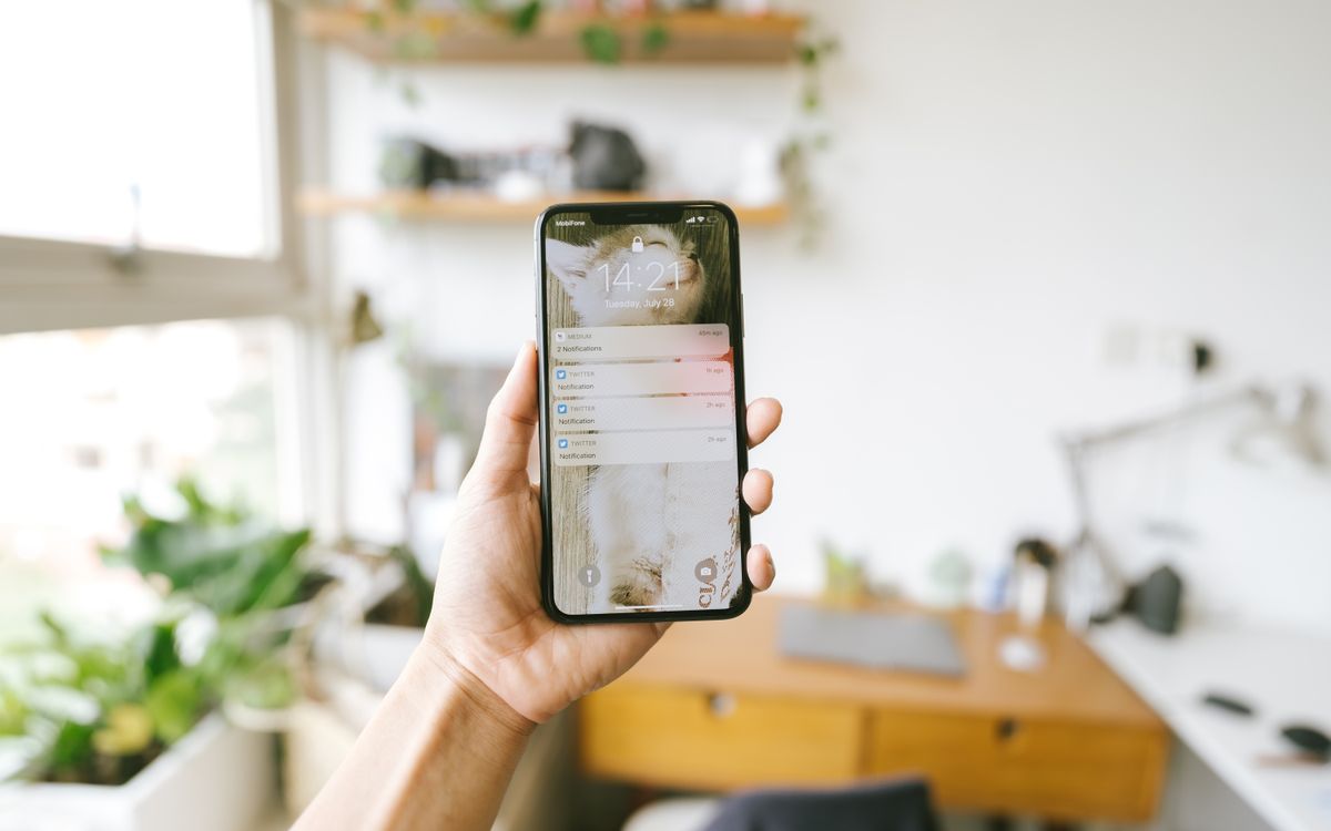 Hand holding smartphone indoors with blurred office background, focus on screen notifications.