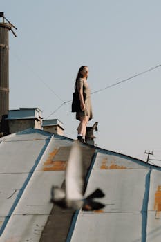 Woman on rooftop in urban setting, with clear sky and city view, expressing freedom and exploration.