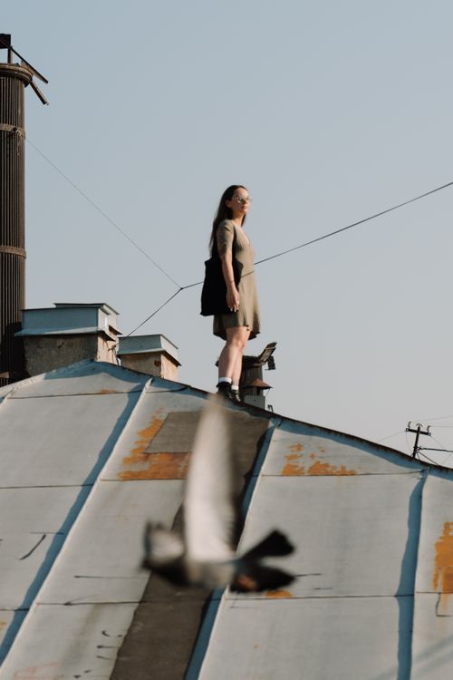 Free Woman on rooftop in urban setting, with clear sky and city view, expressing freedom and exploration. Stock Photo