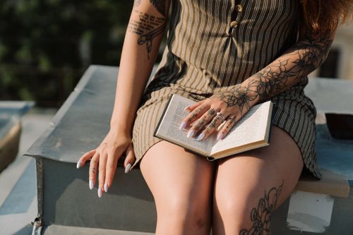 Free Woman with tattoos reading a book on a rooftop, enjoying summer leisure. Stock Photo