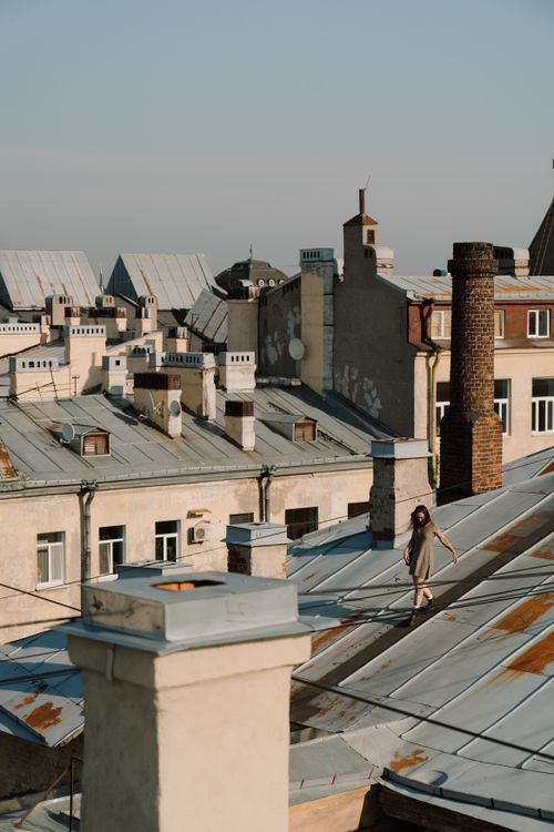 Free Woman walking on historic city rooftops under summer daylight, showcasing urban architecture. Stock Photo