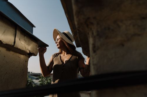 Free Woman with hat enjoys daylight on a city rooftop, capturing urban summer leisure. Stock Photo