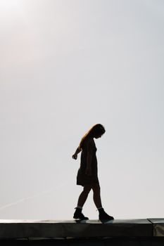 夏日晴朗的天空下，一名身着剪影的女子沿着屋顶行走，唤起自由与探索之感