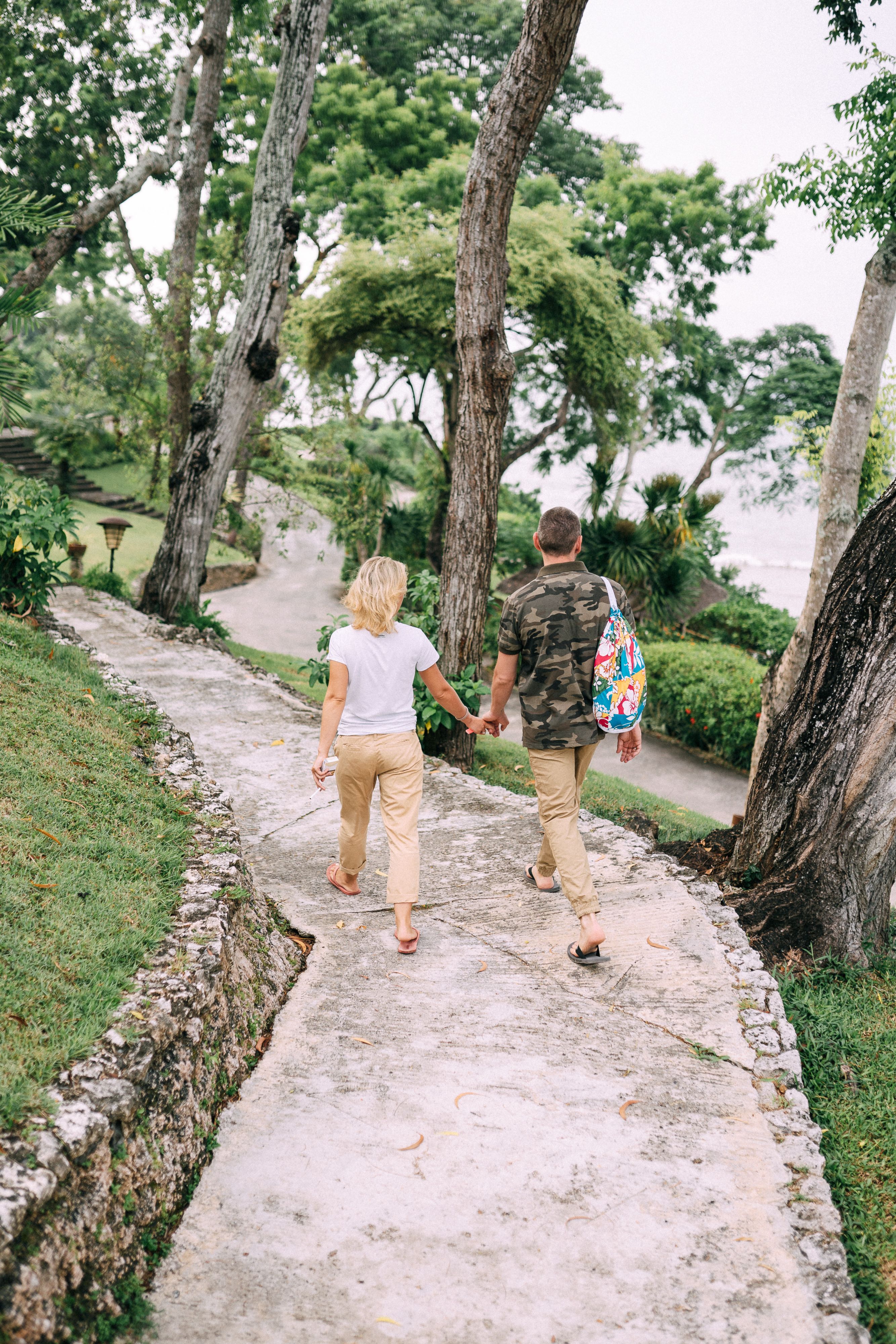 A couple holds hands while walking down a scenic forest path, embracing nature's tranquility.