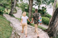 A couple holds hands while walking down a scenic forest path, embracing nature's tranquility.