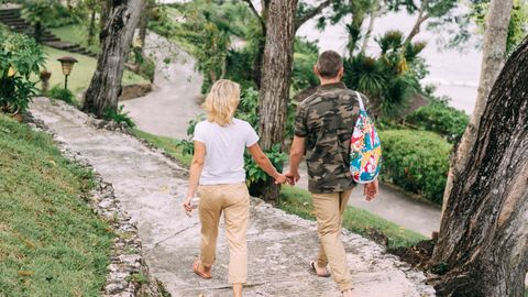 A couple holds hands while walking down a scenic forest path, embracing nature's tranquility.