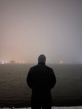 穿着冬衣的人凝视着降雪中雾气弥漫的海洋，透出孤独与宁静