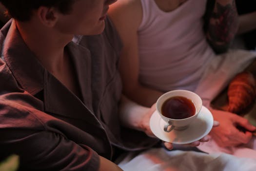 Intimate morning scene of two people enjoying tea and croissants in bed.
