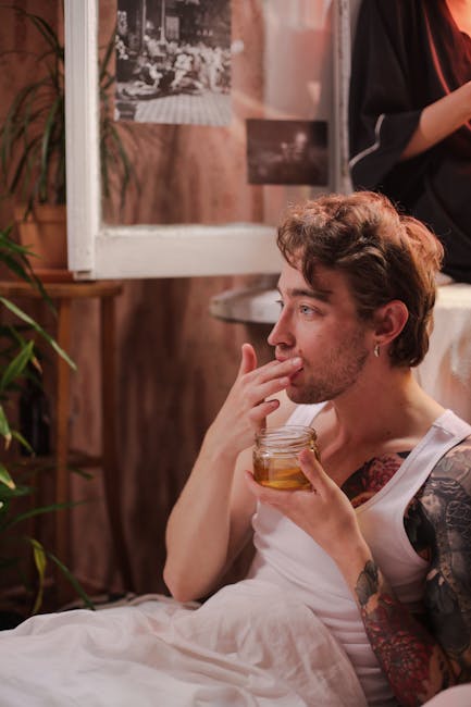 A man with tattoos enjoys honey indoors, surrounded by a cozy setting.