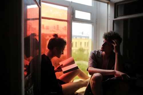 Free A couple enjoys a peaceful reading session by a window with colorful lighting. Indoors and relaxed. Stock Photo