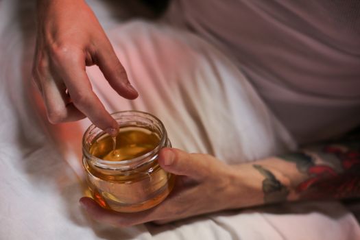 A tattooed person dips a finger into a honey jar, capturing a sweet and tactile moment.