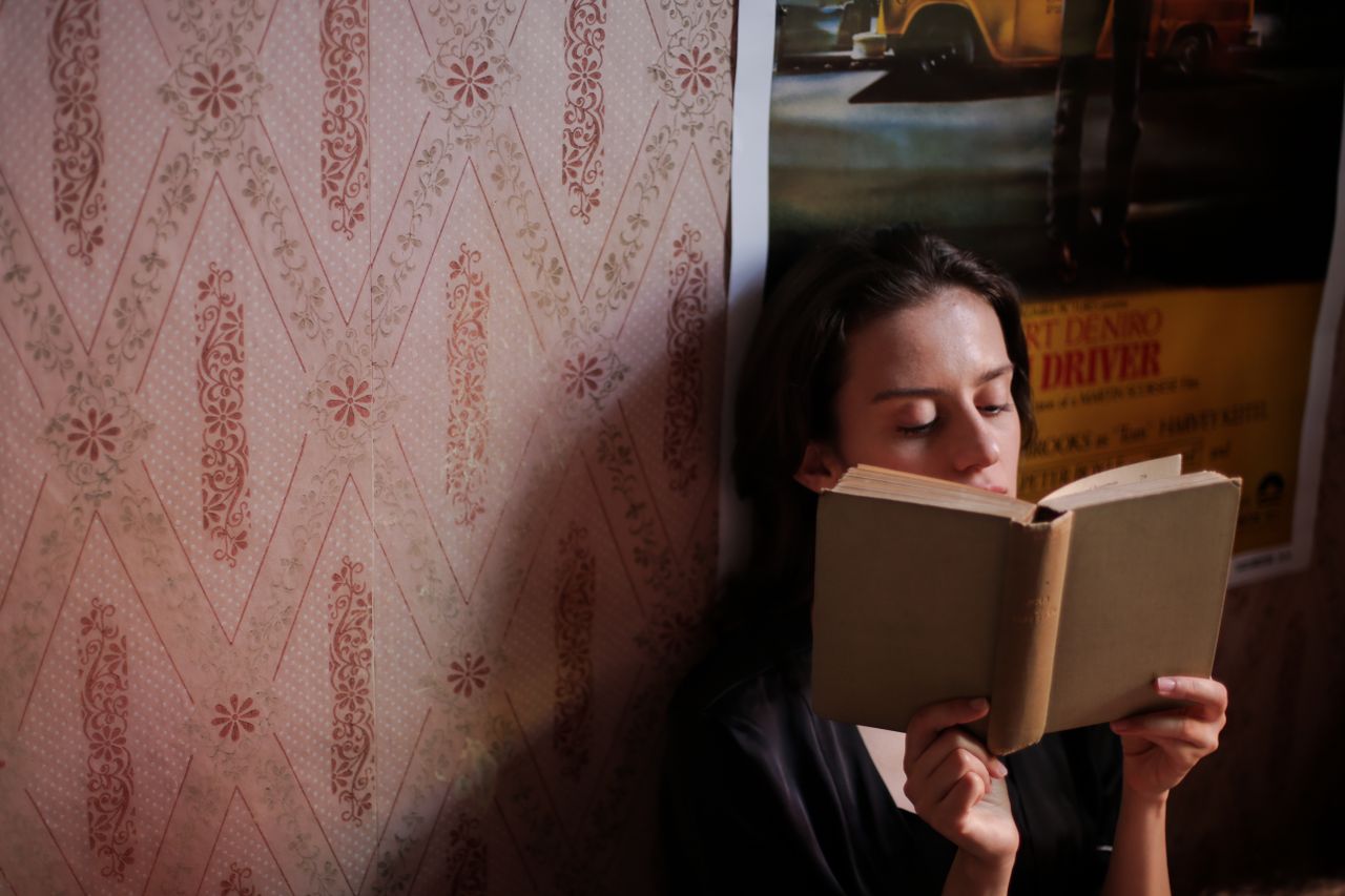 a young woman deeply engrossed in a book surrounded by vintage wallpap