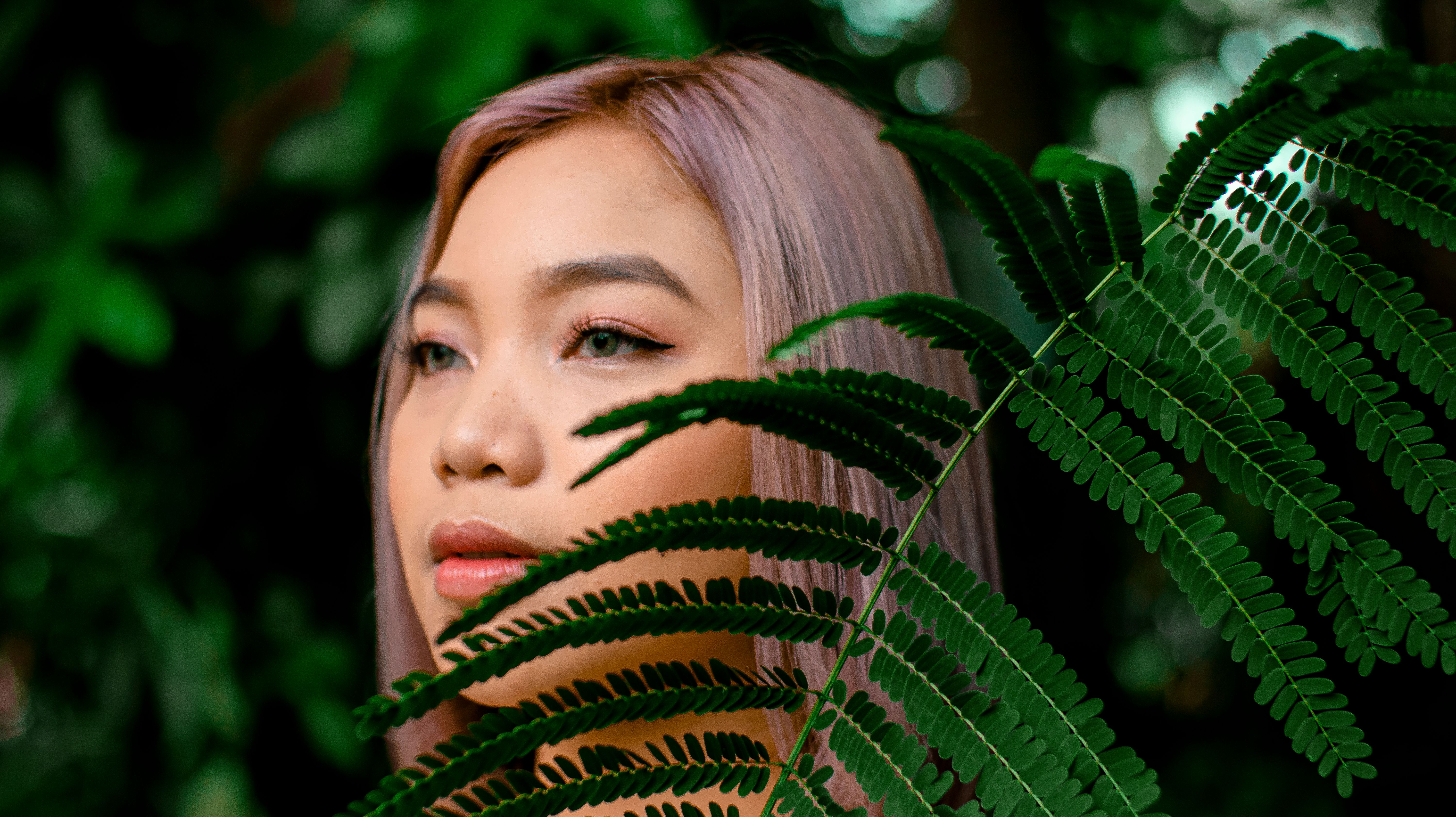 一位粉红色头发的女人正透过户外郁郁葱葱的蕨类植物叶子窥视
