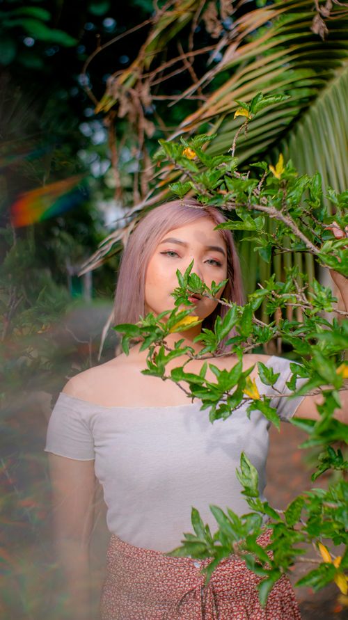 Free A woman stands behind lush greenery, blending into the vibrant outdoor environment. Stock Photo