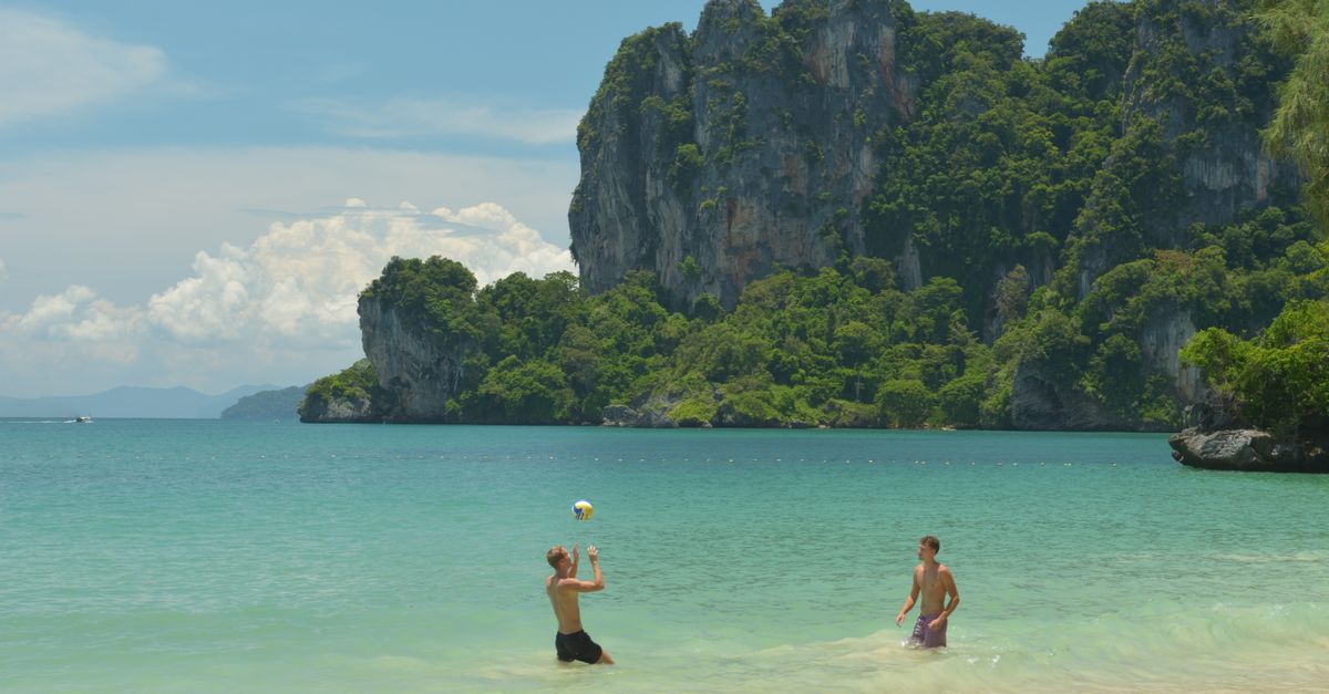 Two men enjoy a game of beach volleyball on Ao Nang's sandy shores with stunning limestone cliffs in the background.