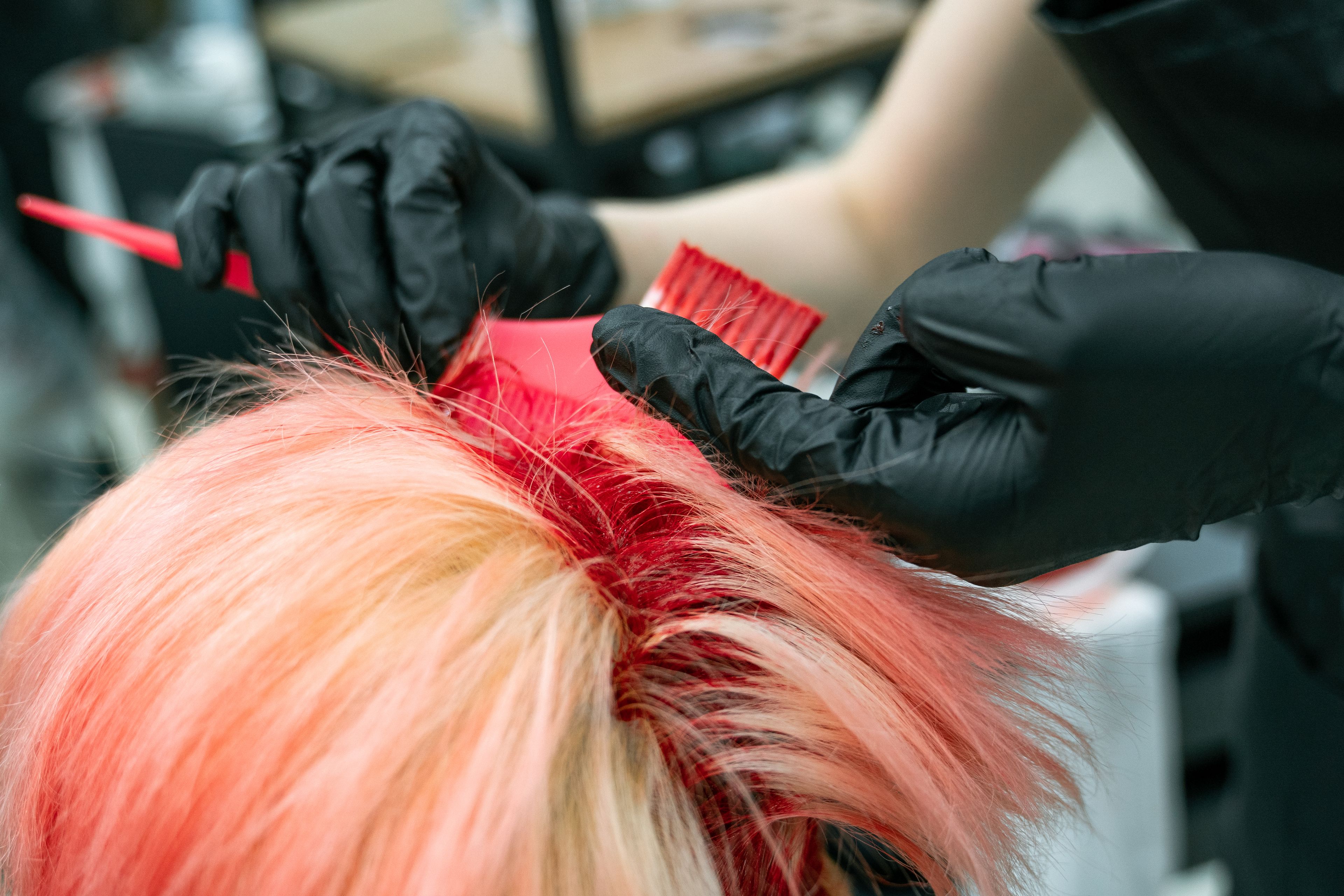 A gloved colourist brushing rose-pink tint through blonde hair