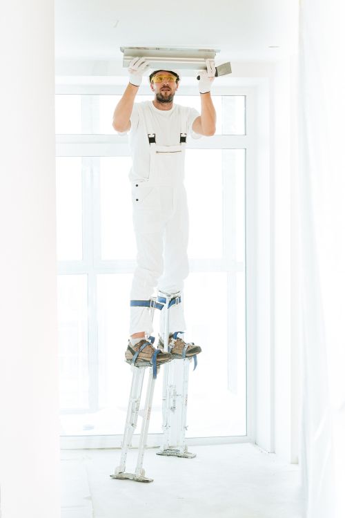Worker on stilts plastering a high ceiling inside a commercial space