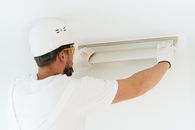 在现代室内环境中，一名穿着安全装备的建筑工人正在安装灯具