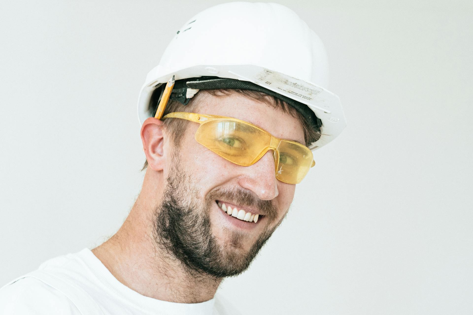 A close-up portrait of a smiling male construction worker wearing safety gear, including a hard hat and goggles.