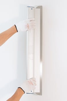 Hands of a worker smoothing a wall with a tool, wearing gloves, close-up on white background.