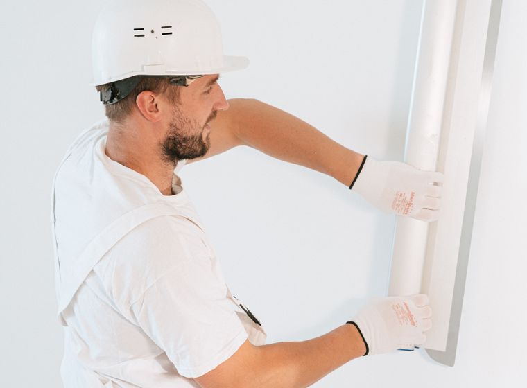 Worker in gloves and helmet installing drywall