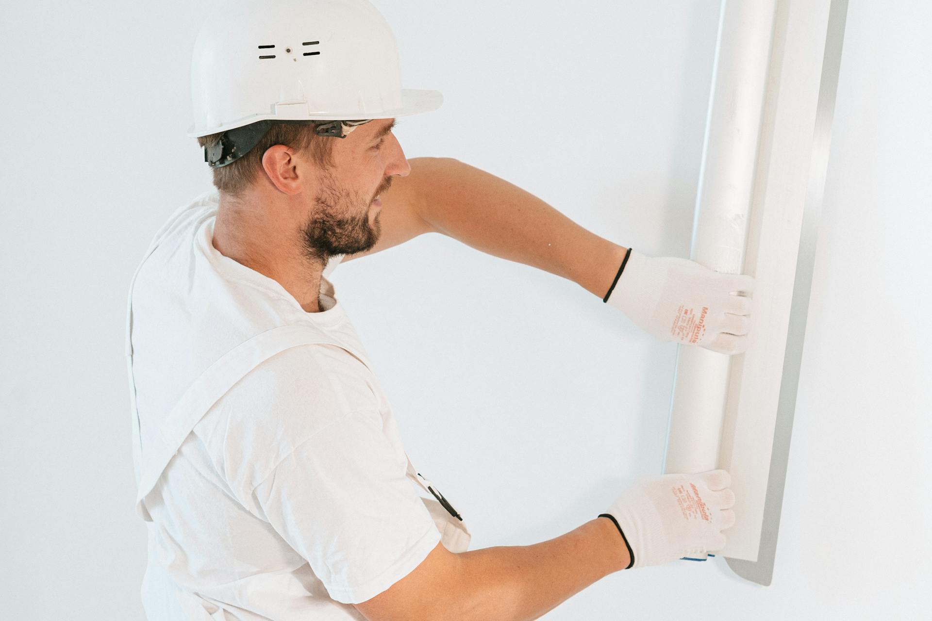 Professional construction worker installing drywall with gloves and helmet inside a building.