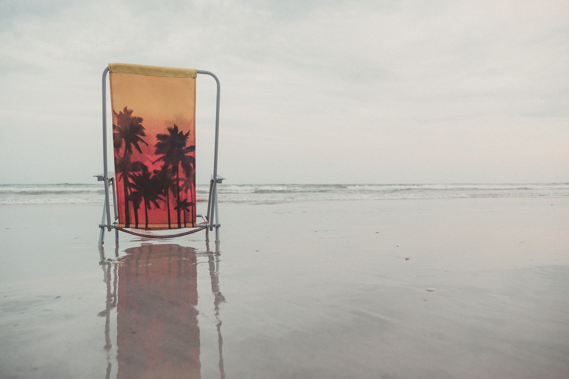 A folding chair with palm tree design on North Topsail Beach, NC, USA, offering a serene seaside view.
