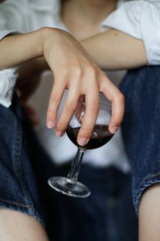一名女子穿着牛仔裤，在室内手持一杯红酒的特写，营造出时尚轻松的氛围