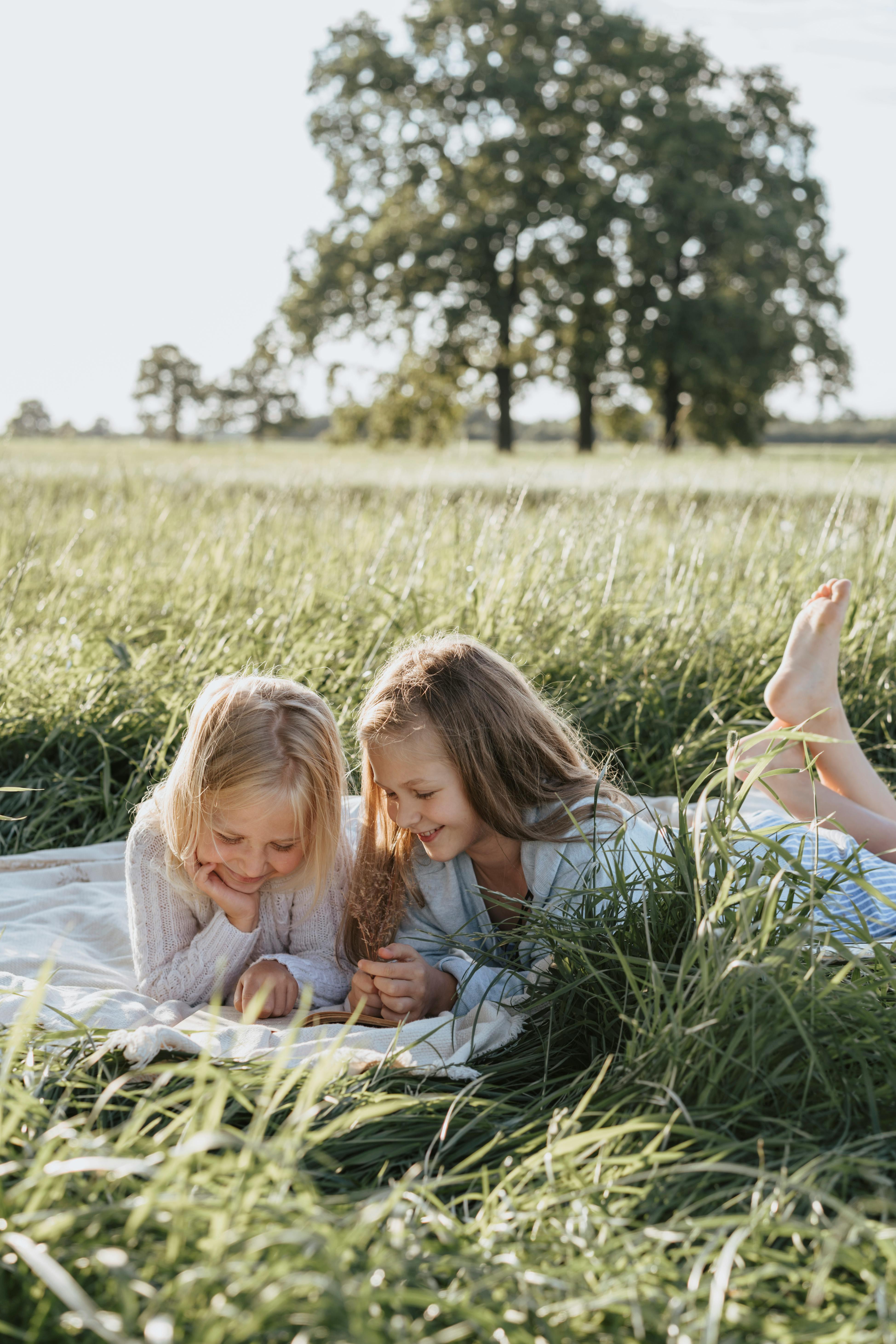 girls lying on white blanket on green grass field