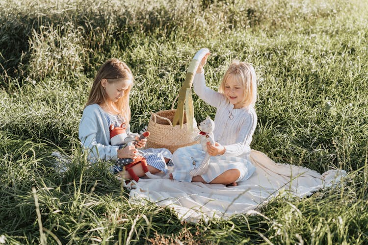 2 Girls Sitting And Playing On A Field