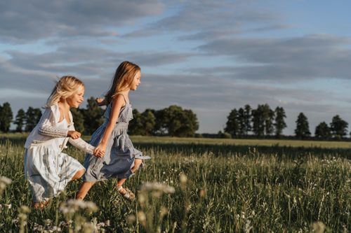 Free Two happy young sisters running hand in hand through a sunlit meadow. Stock Photo
