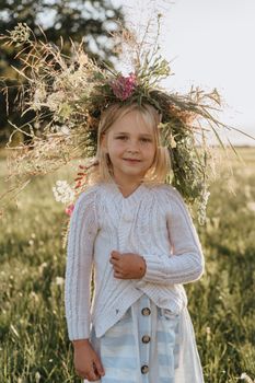 A smiling girl with a floral wreath standing in a sunlit field, capturing a beautiful summer moment.