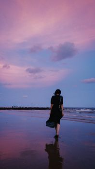 Silhouette of woman walking on beach during a pink and blue sunset, reflecting in the water.