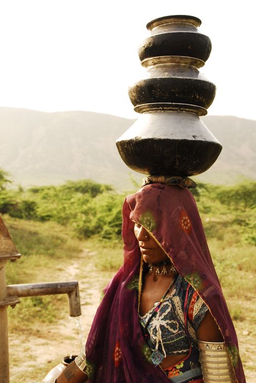 Free A woman in traditional attire balances pots on her head in a rural setting. Stock Photo