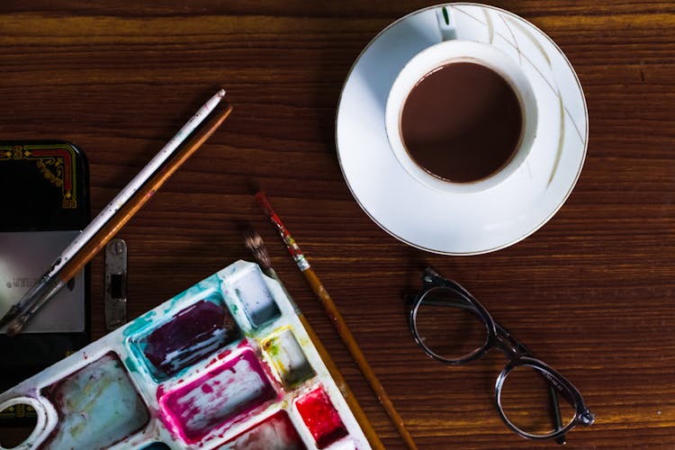 Cup Of Coffee Near Watercolor Palette And Eyeglasses