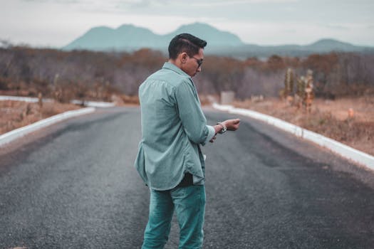 A man in denim stands on an empty road with distant mountains.