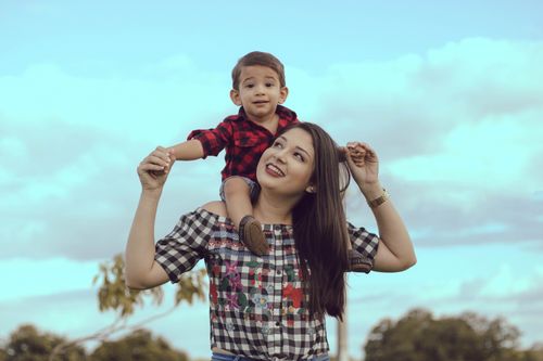 Free A joyful moment as a mother carries her son on her shoulders under a blue sky. Stock Photo